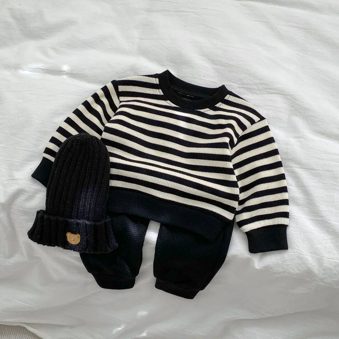 Black and white striped baby outfit with matching black knit beanie on white fabric