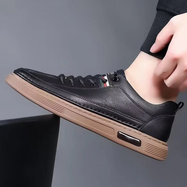 Black leather casual sneaker with brown sole and lace-up design worn on foot against gray background