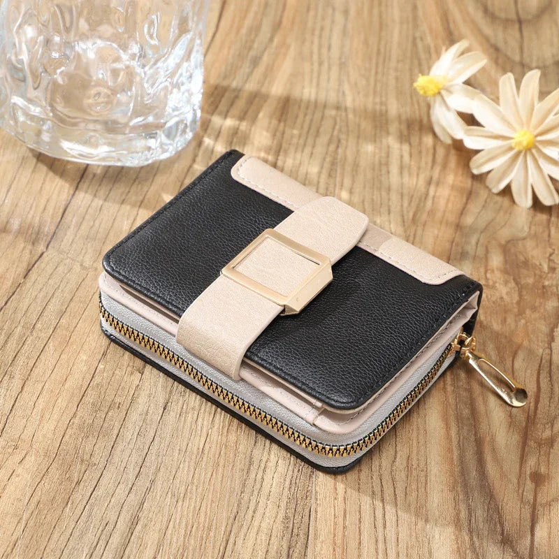 Compact black and beige leather wallet with gold buckle and zipper on wooden table