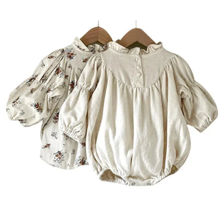 Two baby girls long sleeve rompers on hangers, one plain cream and one floral print cotton fabric