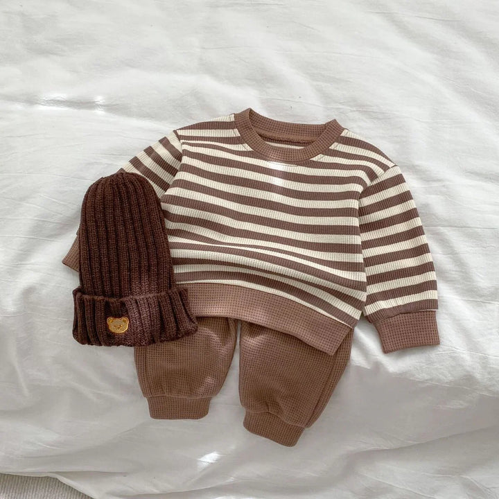 Brown and cream striped toddler outfit with pants and a brown knit beanie on white fabric
