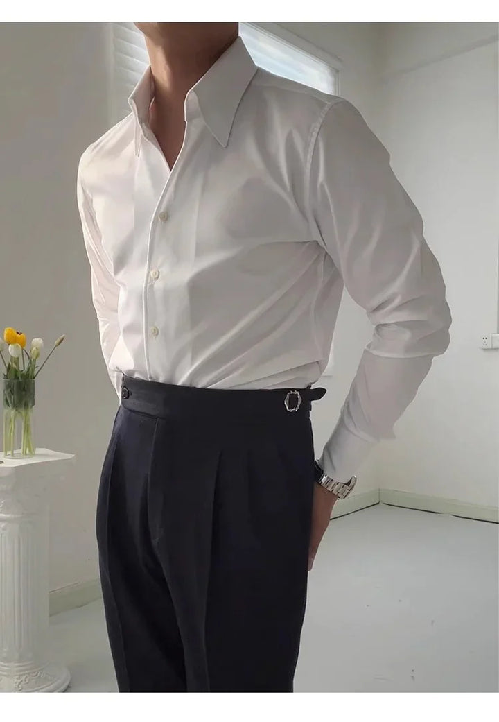 Man wearing white dress shirt and black tailored trousers in a minimalistic white room with a vase of yellow tulips