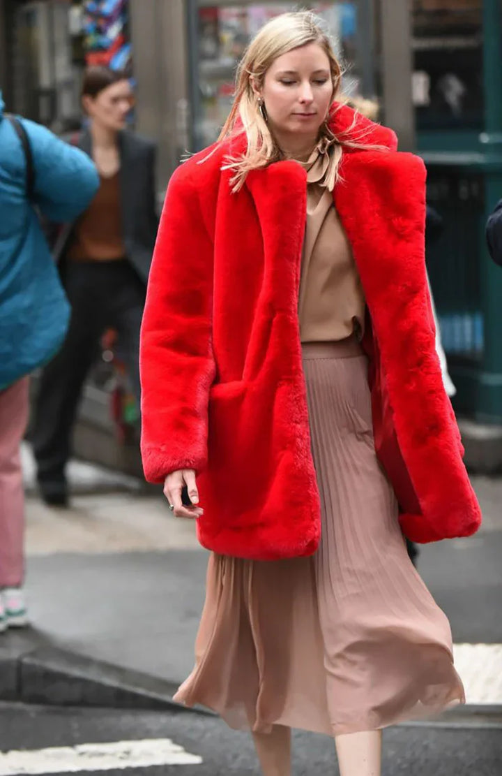 Woman walking on city street wearing a bright red faux fur coat and beige pleated skirt