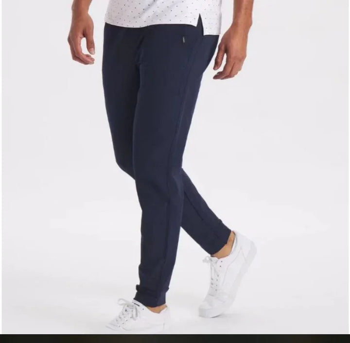 Man wearing navy blue slim fit joggers with white sneakers and a white shirt on a white background