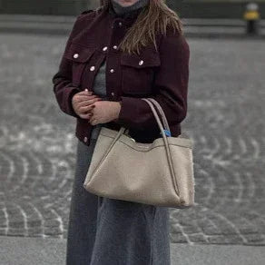 Woman in burgundy jacket carrying beige leather handbag on cobblestone street