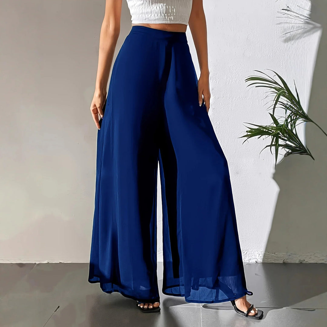 Woman wearing high-waisted navy wide-leg pants and white cropped top in minimal indoor setting