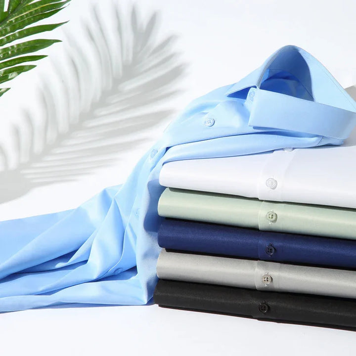 Stack of neatly folded dress shirts in blue, white, green, navy, gray, and black with a palm leaf shadow