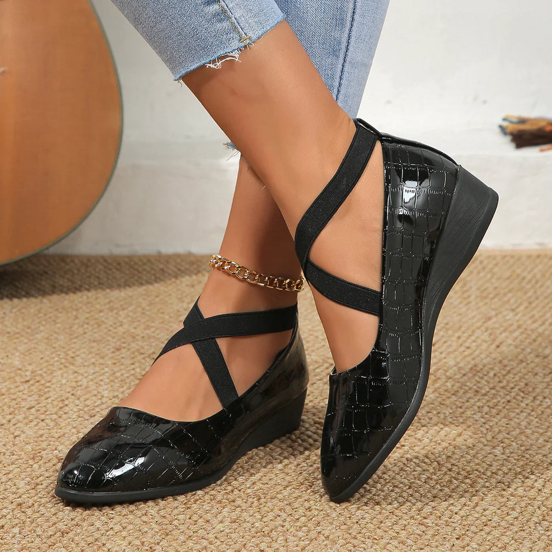 Black patent wedge shoes with croc texture and crisscross straps worn with light blue jeans and gold anklet