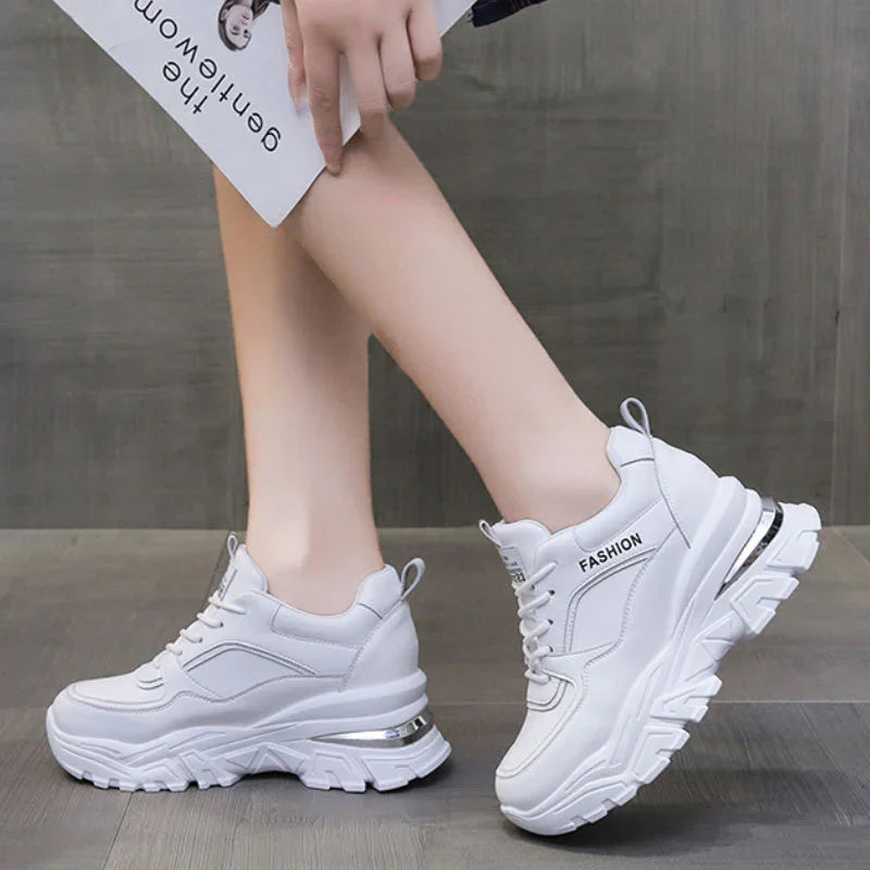 White fashion sneakers with chunky sole worn on feet against gray floor and wall