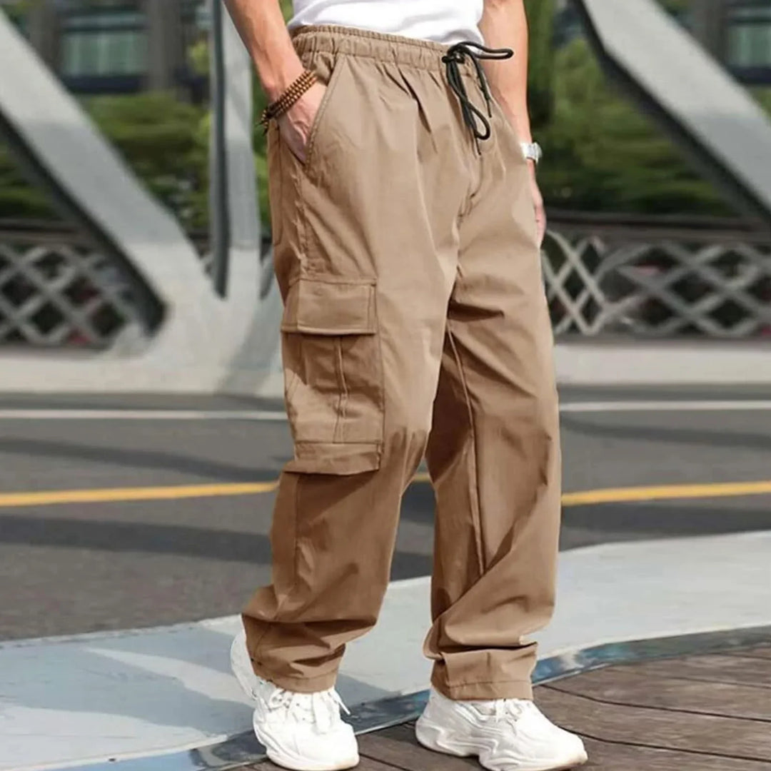 Man wearing beige cargo pants with drawstring waist and white sneakers standing outdoors