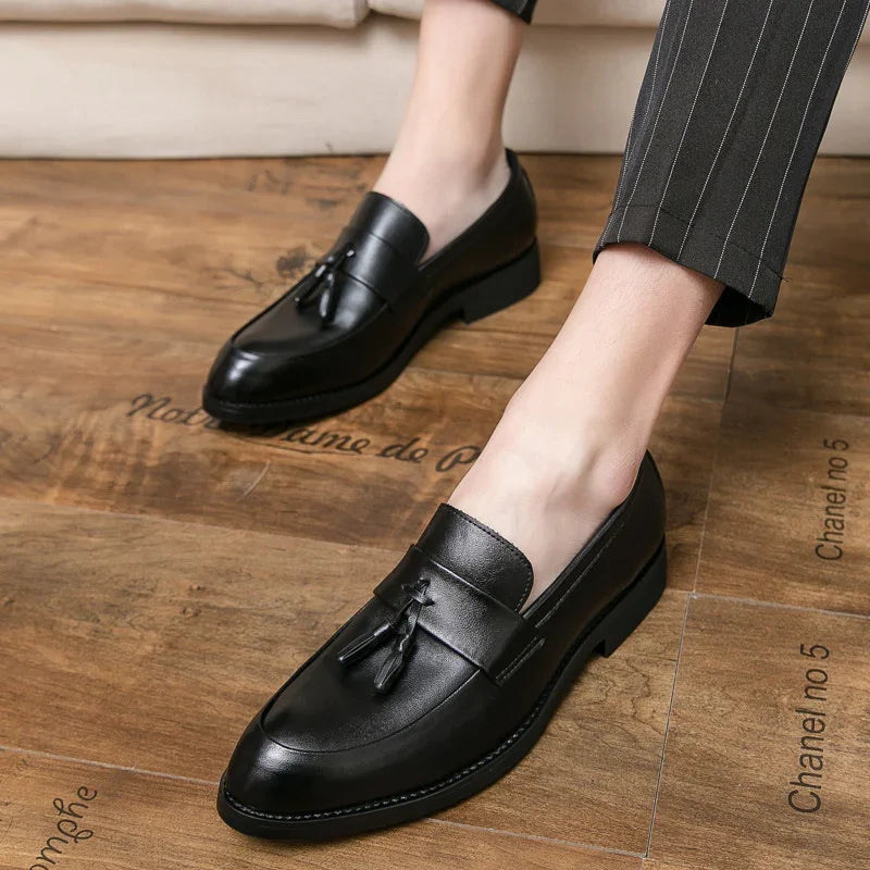 Close-up of stylish black leather tassel loafers worn with pinstriped pants on wooden floor