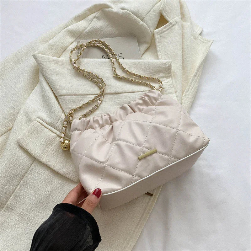 Beige quilted handbag with gold chain strap on cream textured blazer, fashion accessories