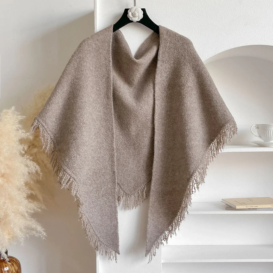 Beige soft wool shawl with fringed edges hanging on black hanger in cozy minimalist room