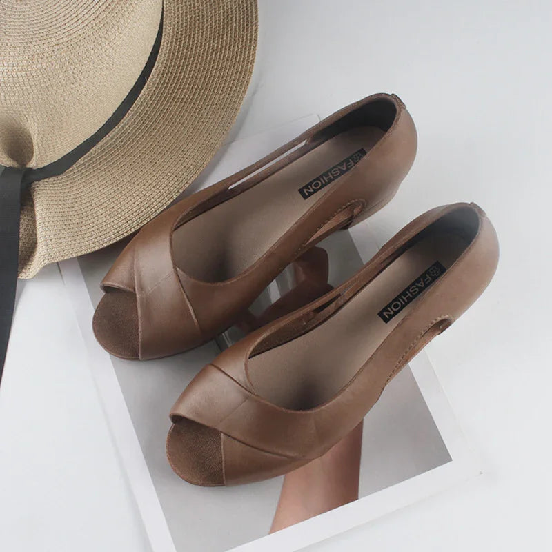 Pair of brown leather peep-toe flats on a white surface next to a beige woven hat with black ribbon