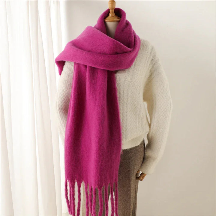 Bright pink fringed scarf on mannequin wearing white textured sweater and brown pants