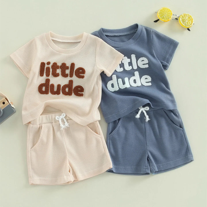 Two toddler short-sleeve sets with shorts, one beige, one blue, both waffle-knit with "little dude" text