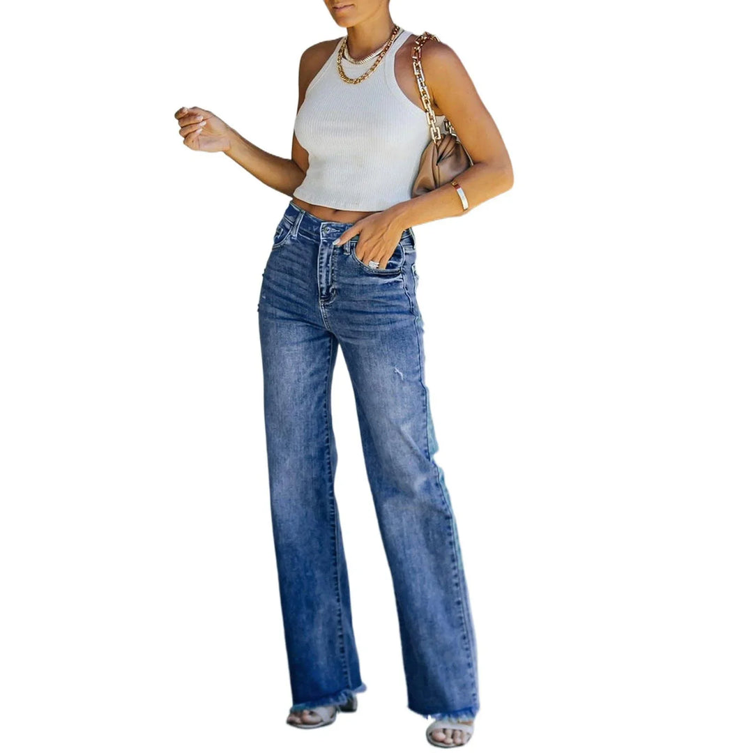 Woman wearing white sleeveless crop top, high-waisted wide-leg blue jeans, gold chain necklace, and tan shoulder bag