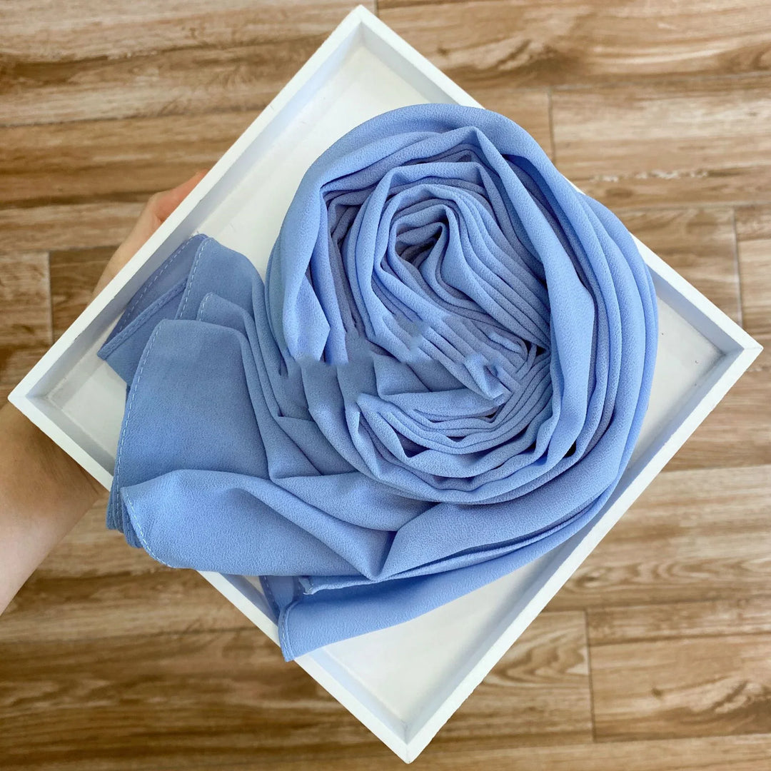 Hand holding white tray with neatly folded light blue chiffon scarf on wooden floor