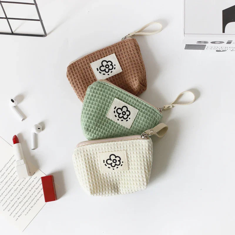 Three waffle-textured zipper pouches in brown, green, and white with flower patch on white surface