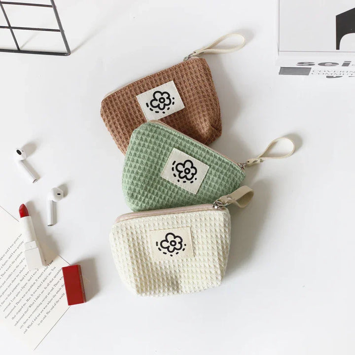 Three waffle-textured zipper pouches in brown, green, and white with flower patch on white surface