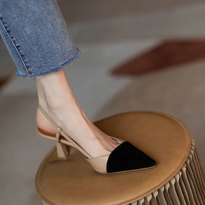 woman wearing beige and black slingback pointed toe heels with low block heel on round brown stool