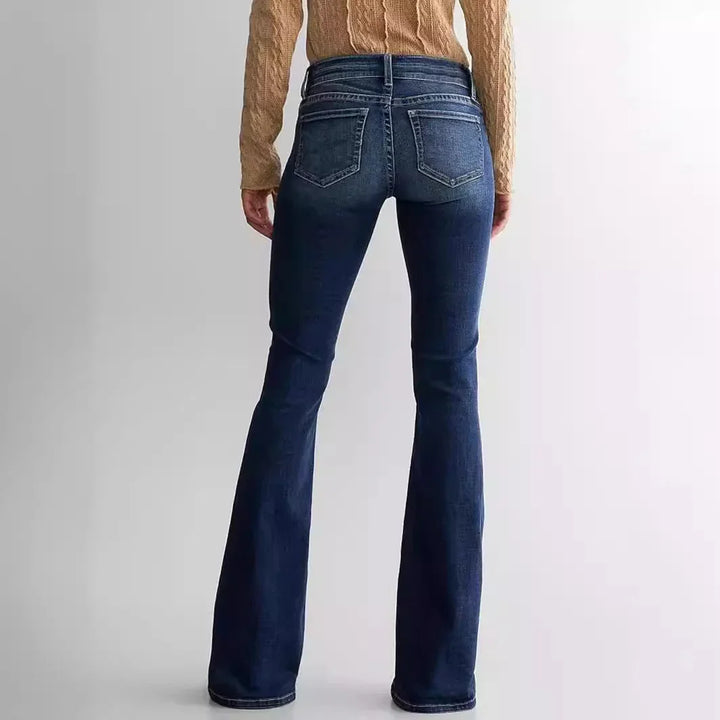 Back view of woman wearing dark blue flare jeans and beige cable knit sweater on plain background