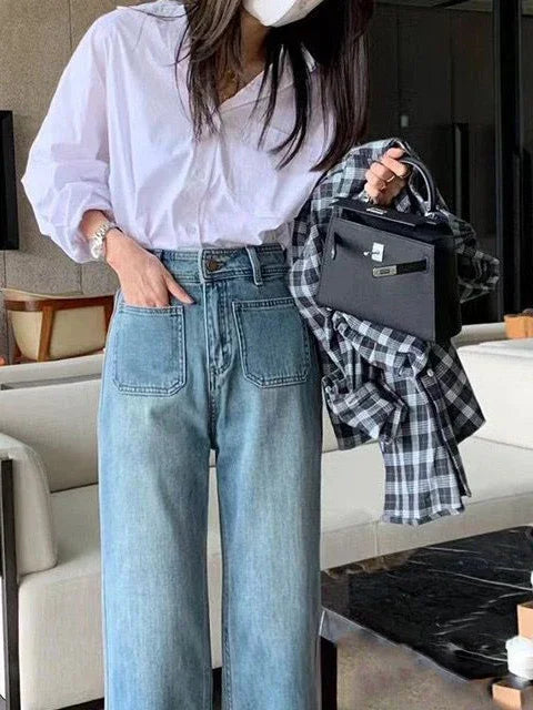 Woman wearing white blouse and high-waisted wide-leg jeans holding black handbag and plaid shirt indoors