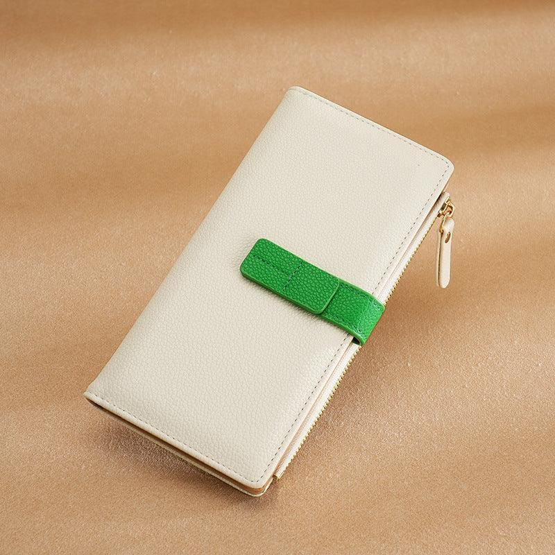 Beige leather wallet with green strap and gold zipper on tan textured surface
