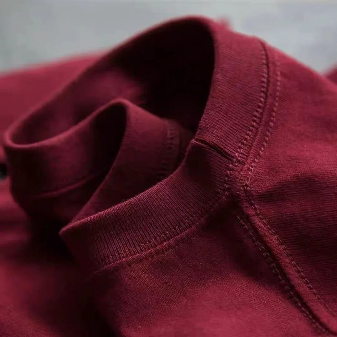 Close-up of a folded maroon cotton sweatshirt showing ribbed collar and stitching details