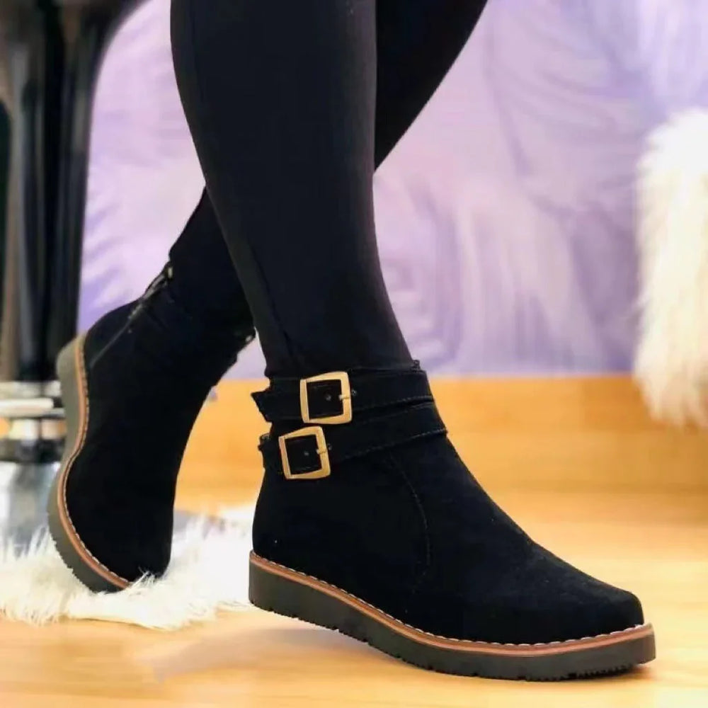 Black suede ankle boots with gold buckles worn with black leggings on wooden floor