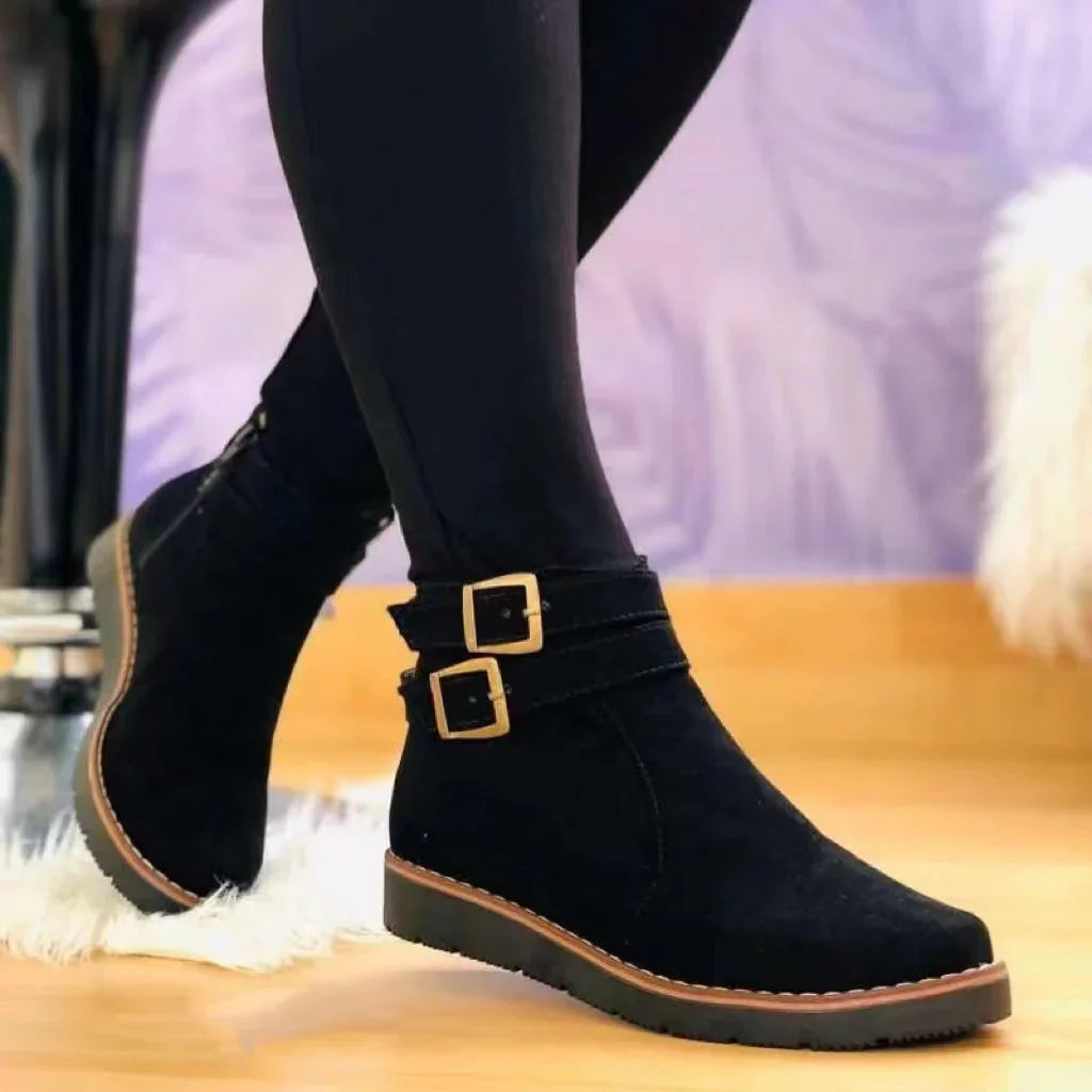 Black suede ankle boots with gold buckles worn with black leggings on wooden floor