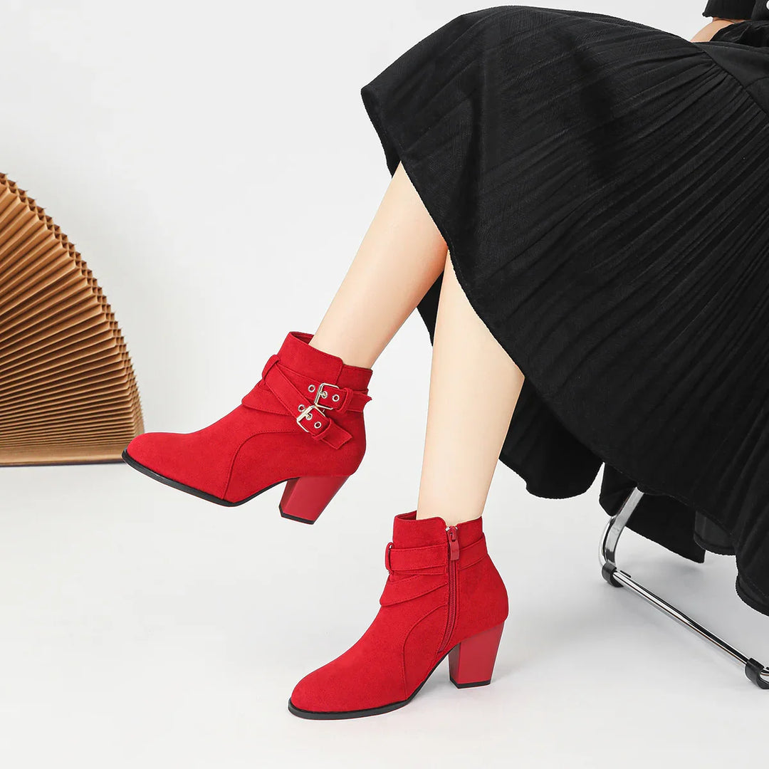 Woman wearing stylish red suede ankle boots with buckles and block heels, paired with a black pleated skirt