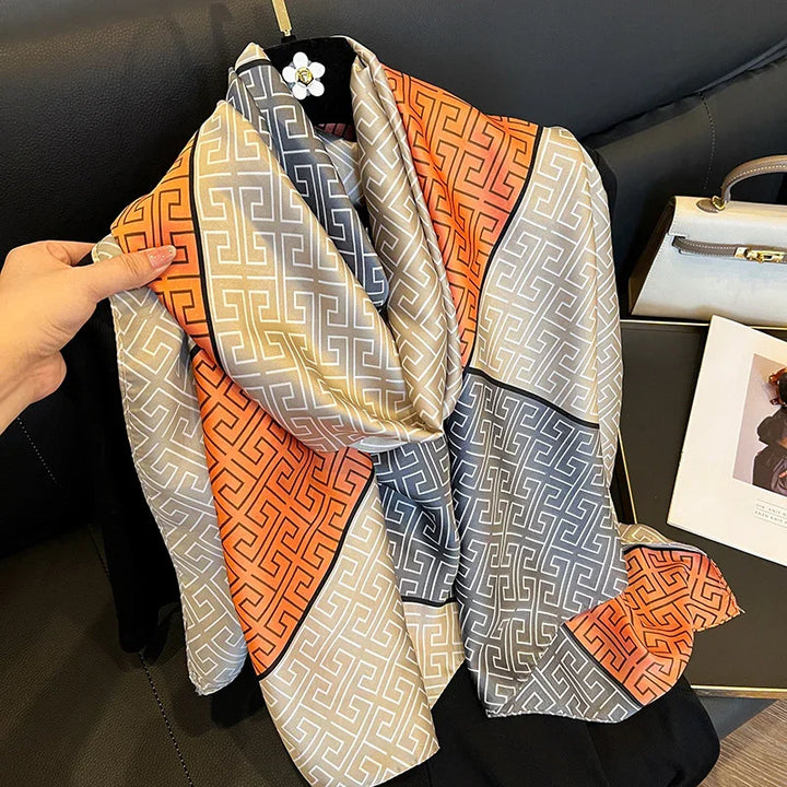 Silk scarf with geometric pattern in orange, beige, and gray draped on black background