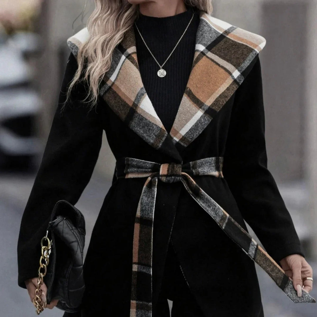 Woman wearing black coat with plaid collar and belt holding black quilted handbag with gold chain