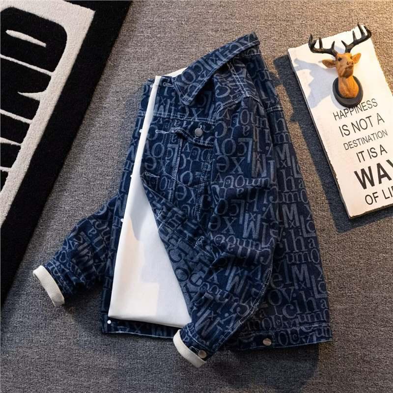 Denim jacket with all-over white text pattern over a white shirt on gray carpet next to a deer head wall decor