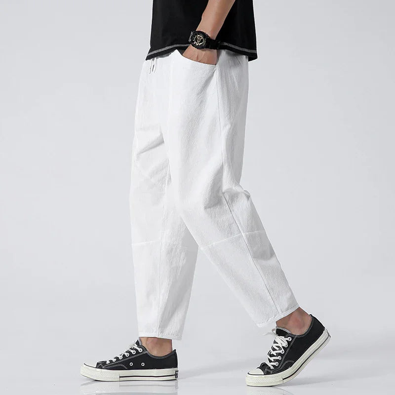 Person wearing white casual pants and black sneakers with white laces on light background
