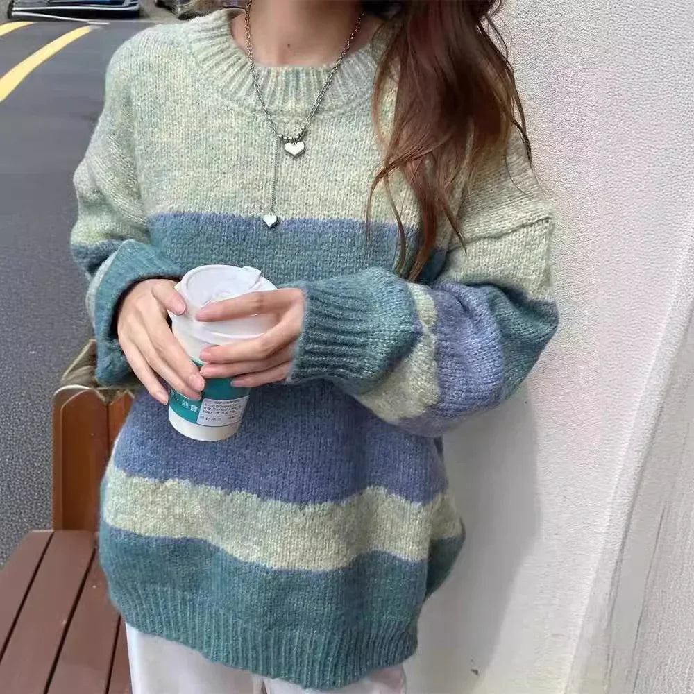 Woman wearing oversized striped knit sweater in blue and green holding a cup outdoors