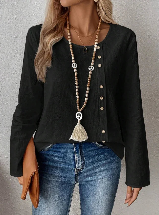Woman wearing black buttoned long sleeve top, blue jeans, peace sign bead necklace, and holding brown clutch