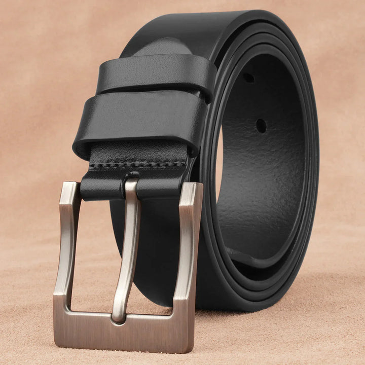 Black leather belt with brushed metal buckle on beige surface, rolled up neatly