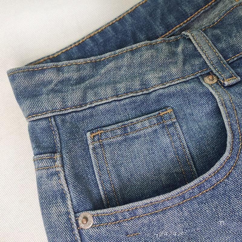 Close-up of blue denim jeans front pocket with contrast stitching and metal rivets on white background