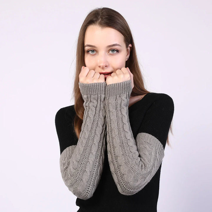 Young woman wearing black sweater with gray cable knit long sleeves, posing with hands near face