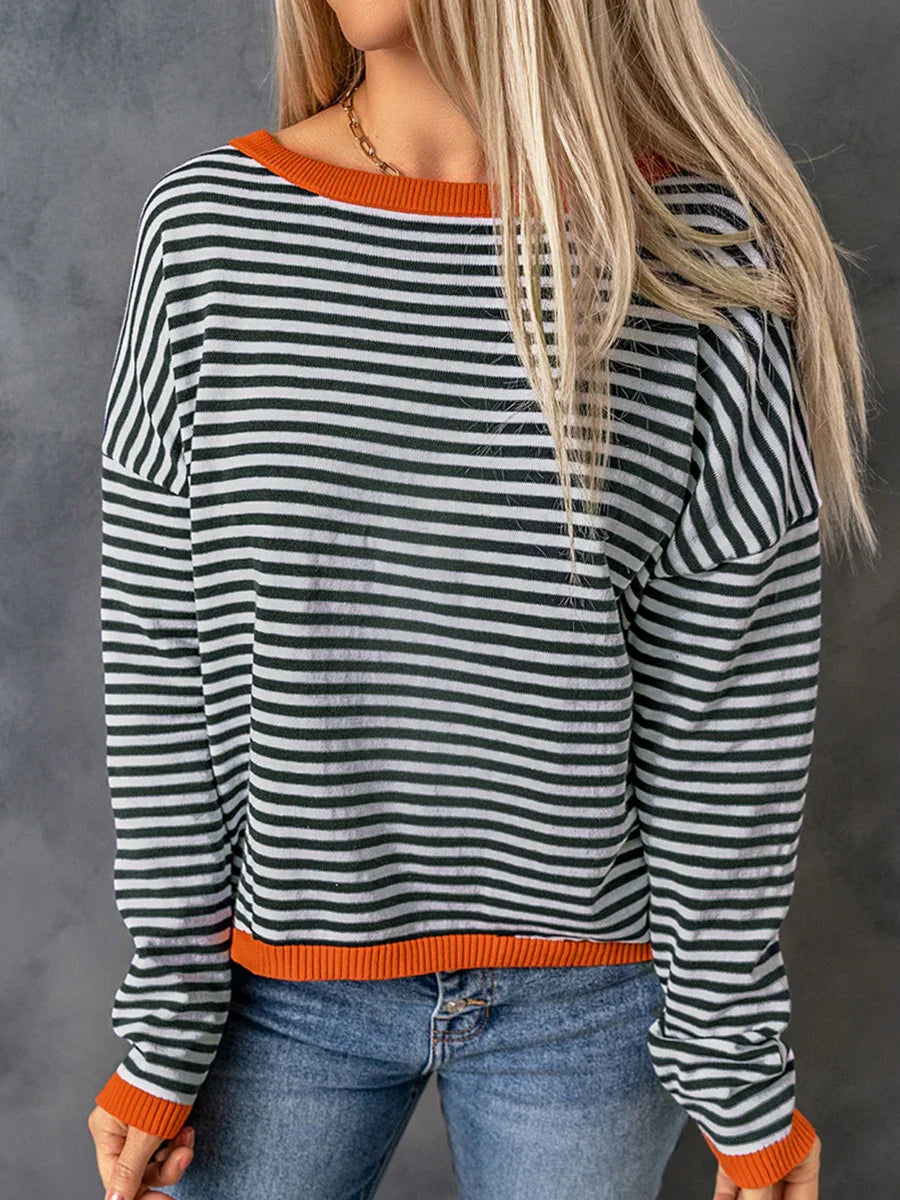 Woman wearing black and white striped sweater with orange trim and blue jeans against gray background