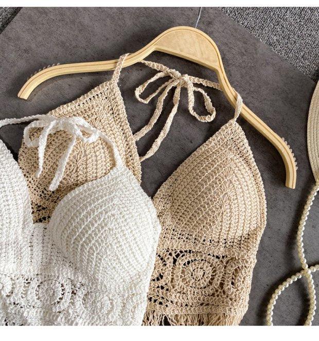 Handmade beige and white crochet halter tops displayed on a wooden hanger on a grey textured surface