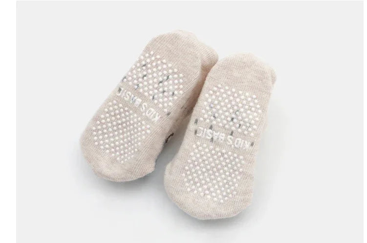 Pair of beige non-slip baby socks with white grip dots on soles, isolated on white background
