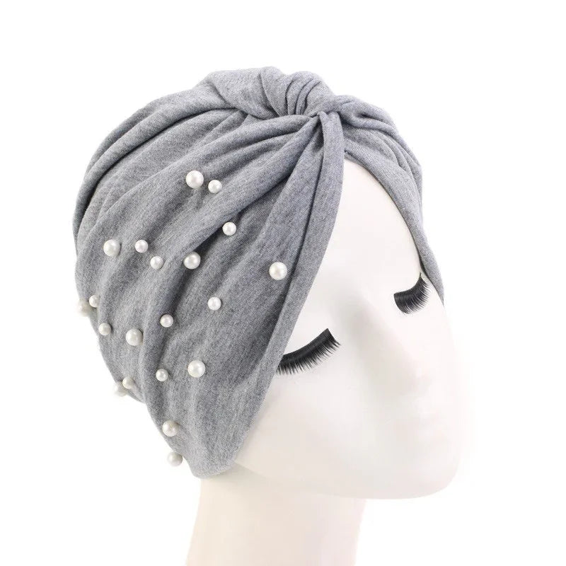 Gray turban headwrap adorned with white pearls on white mannequin head with closed eyes
