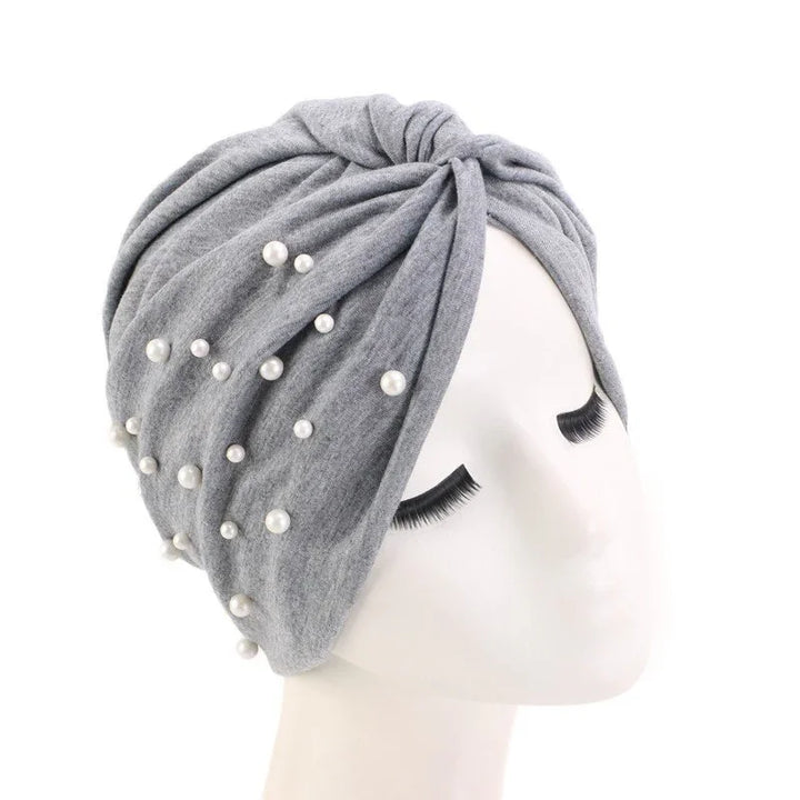 Gray turban headwrap adorned with white pearls on white mannequin head with closed eyes
