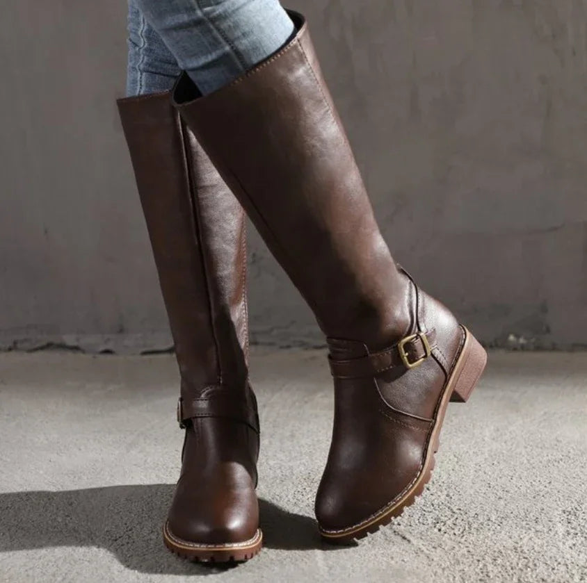Woman wearing brown leather knee-high boots with buckle detail on concrete floor