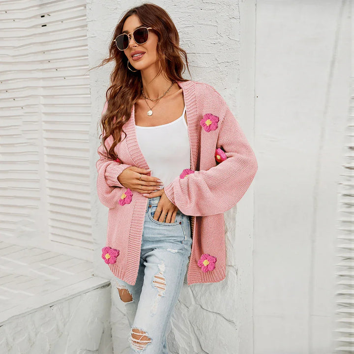 Woman wearing pink knit cardigan with flower appliques, white tank top, ripped jeans, and sunglasses