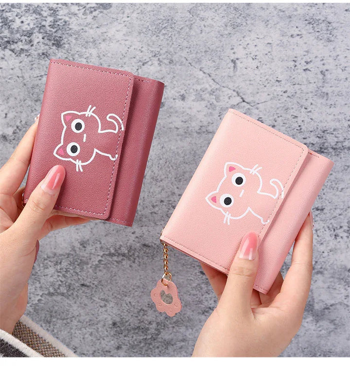 Two pink compact wallets with cute cartoon cat face design held in hands on gray textured background