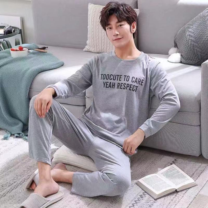 Young man wearing grey pajamas with text sitting on floor near sofa with open book and cozy blanket